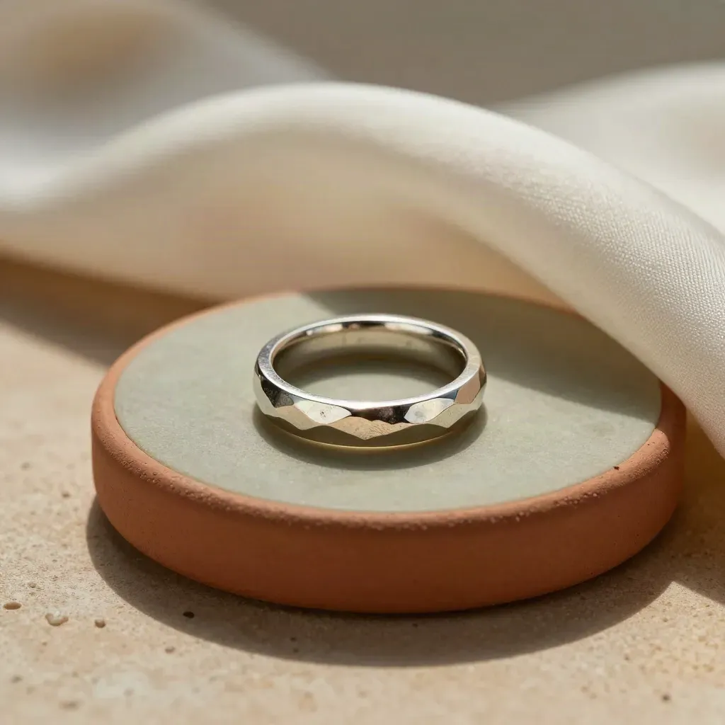Bague martelée en métal clair sur socle minéral, avec soie et ombre nette.